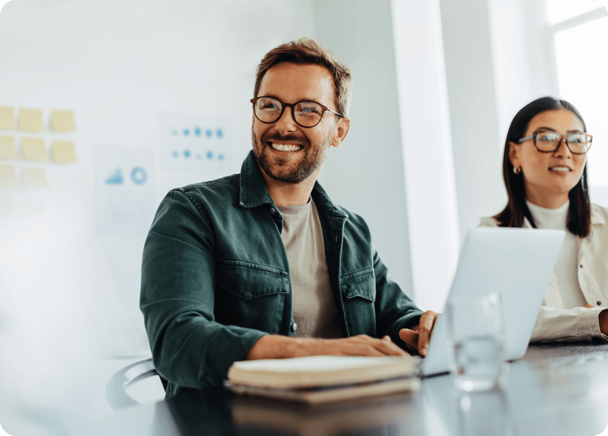 two people in office sitting at a desk in front of a laptop.